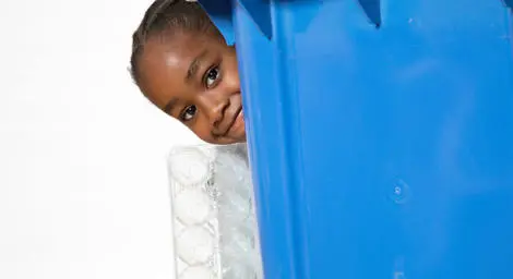 Girl hiding behind blue recycling bin.