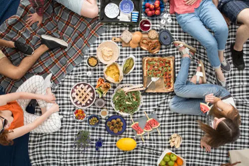 Bird's eye view of four people sitting on picnic blanket surrounded by finger foods