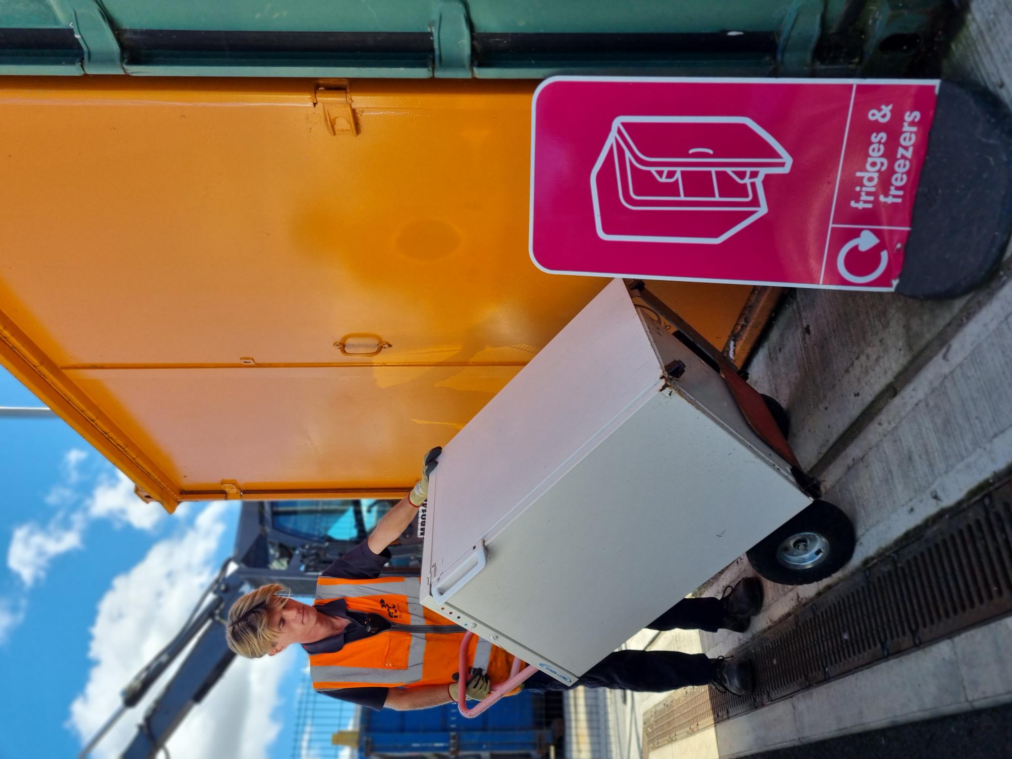 A recycling centre worker moving a white fridge into an orange reuse container