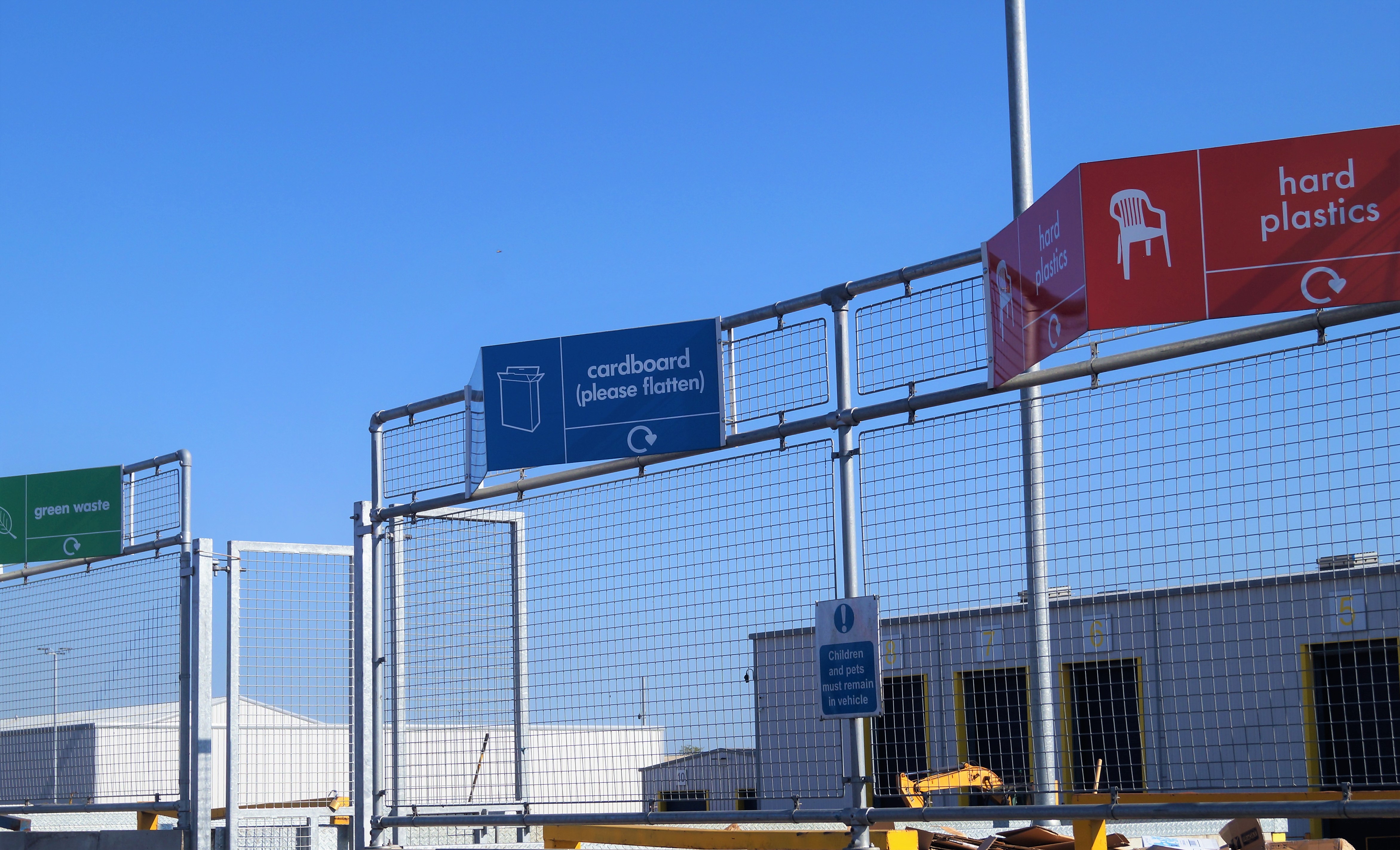 Signs saying garden waste, cardboard and hard plastics at a recycling centre. 